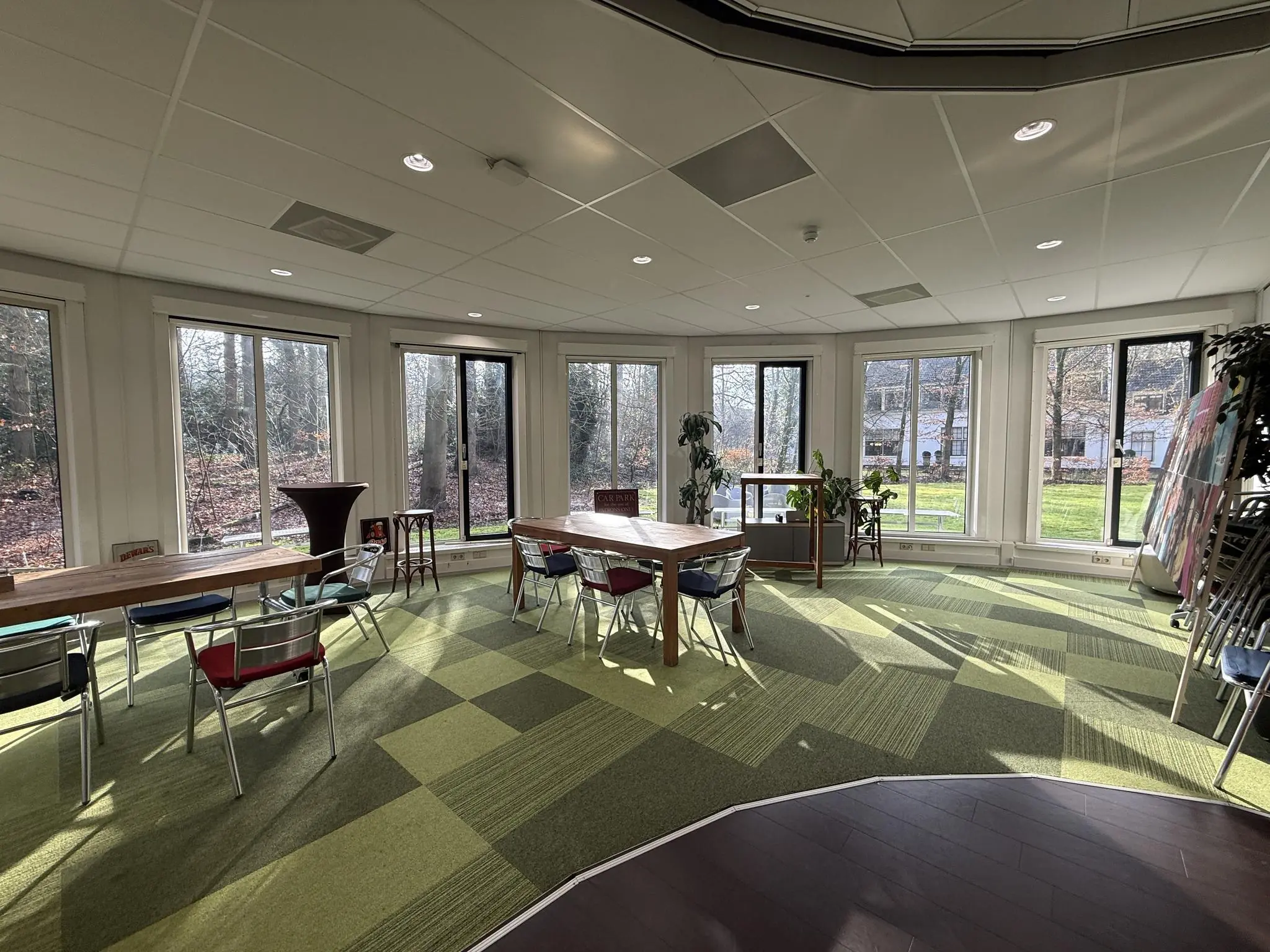 Lichte vergaderruimte aan de Arnhemse Bovenweg met groene vloerbedekking, grote ramen en uitzicht op een bosrijke omgeving.